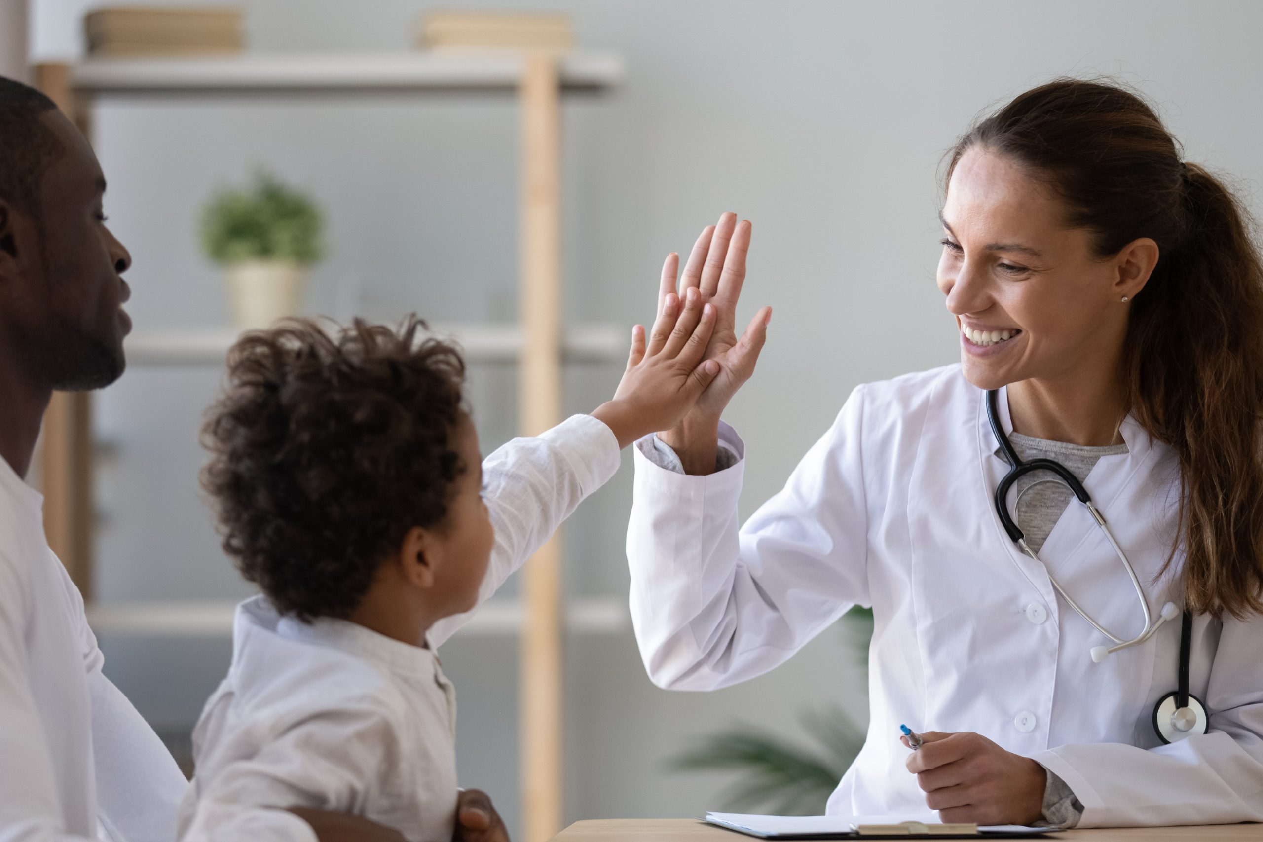 Smiling young female pediatrician give high five to little african American boy at consultation in clinic, happy woman doctor consult biracial toddler kid in hospital.